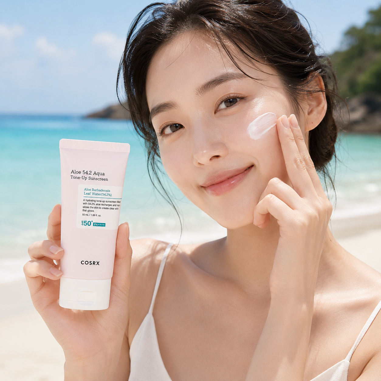 A woman on a sunny beach holds a tube of COSRX Aloe 142 Aqua True-Glow Intensive Sun Protection Factor 150 sunscreen while applying cream to her face.