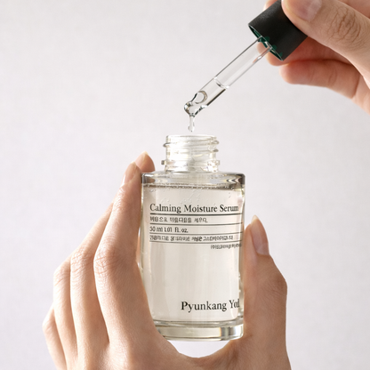 Calming moisture serum being dripped from a dropper into a clear bottle labeled 'Pyunkang Yul' on a light gray background.